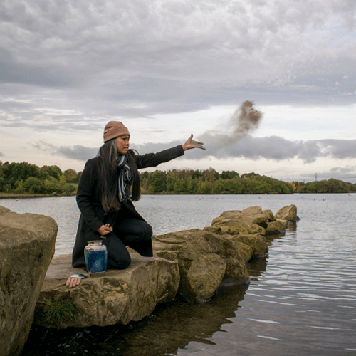 Woman kneeling and spreading ashes over water